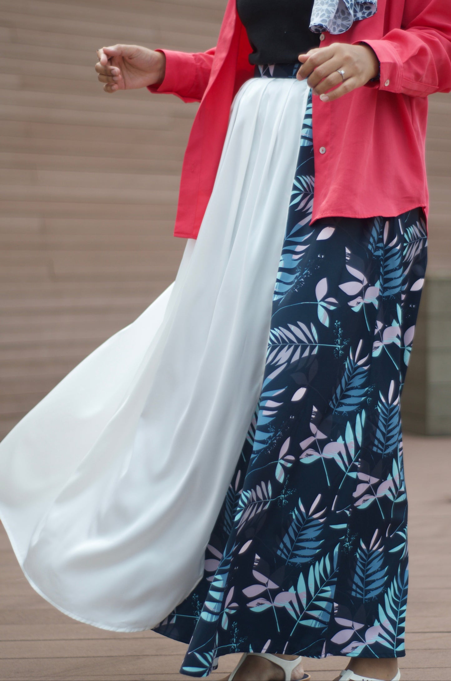 Person wearing a hijab, pink shirt, and navy floral SKIRT against a neutral background